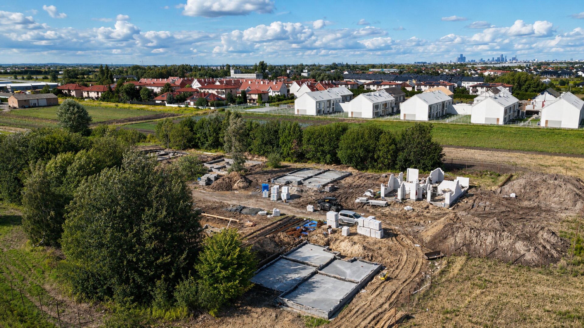 Widok z lotu ptaka na budowę osiedla z panoramą Warszawy w tle